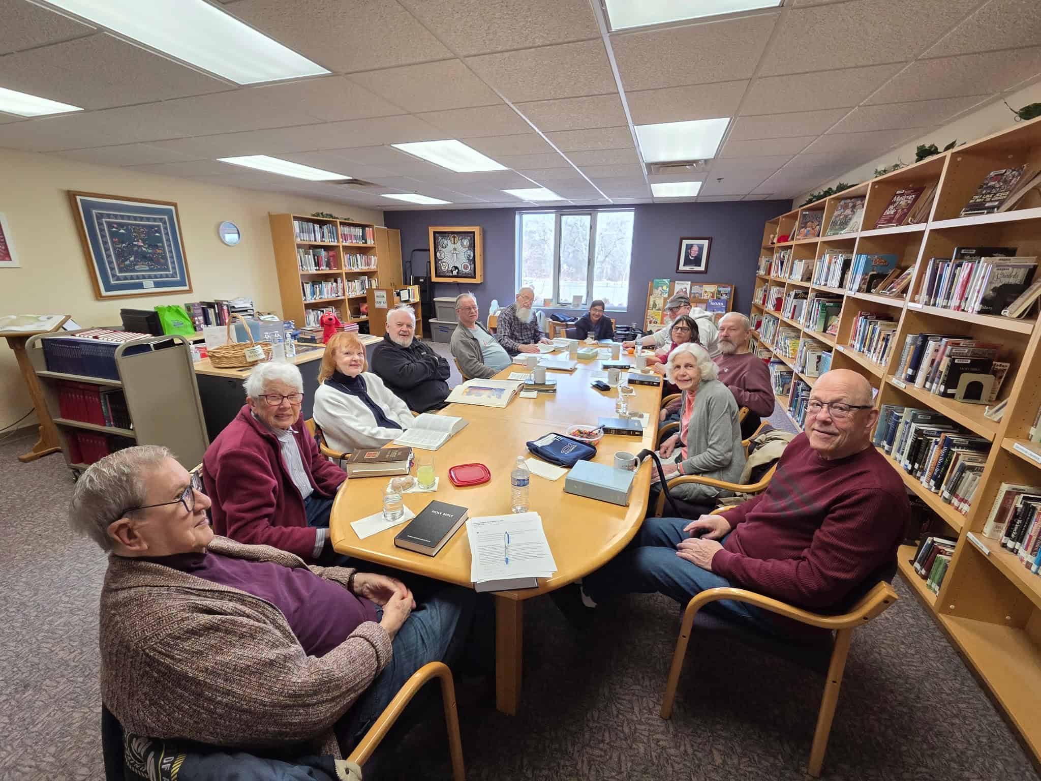 Group of elderly people gathered around a table in a library, engaging in a meeting or discussion.